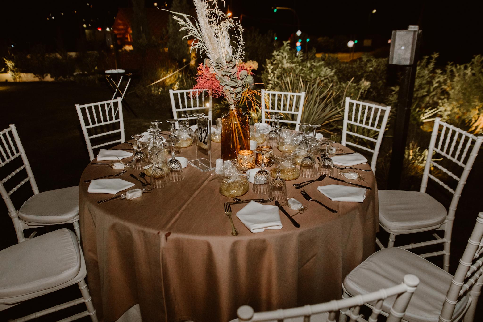 Κοντινή φωτογραφία από το τραπέζι που έχει στήσει το catering με γυάλινα ποτήρια και μαχαιροπίρουνα. Στο κέντρο έχει τον στολισμό ο οποίος αποτελείτε από pampas mpez και φούξια και πρασινάδες