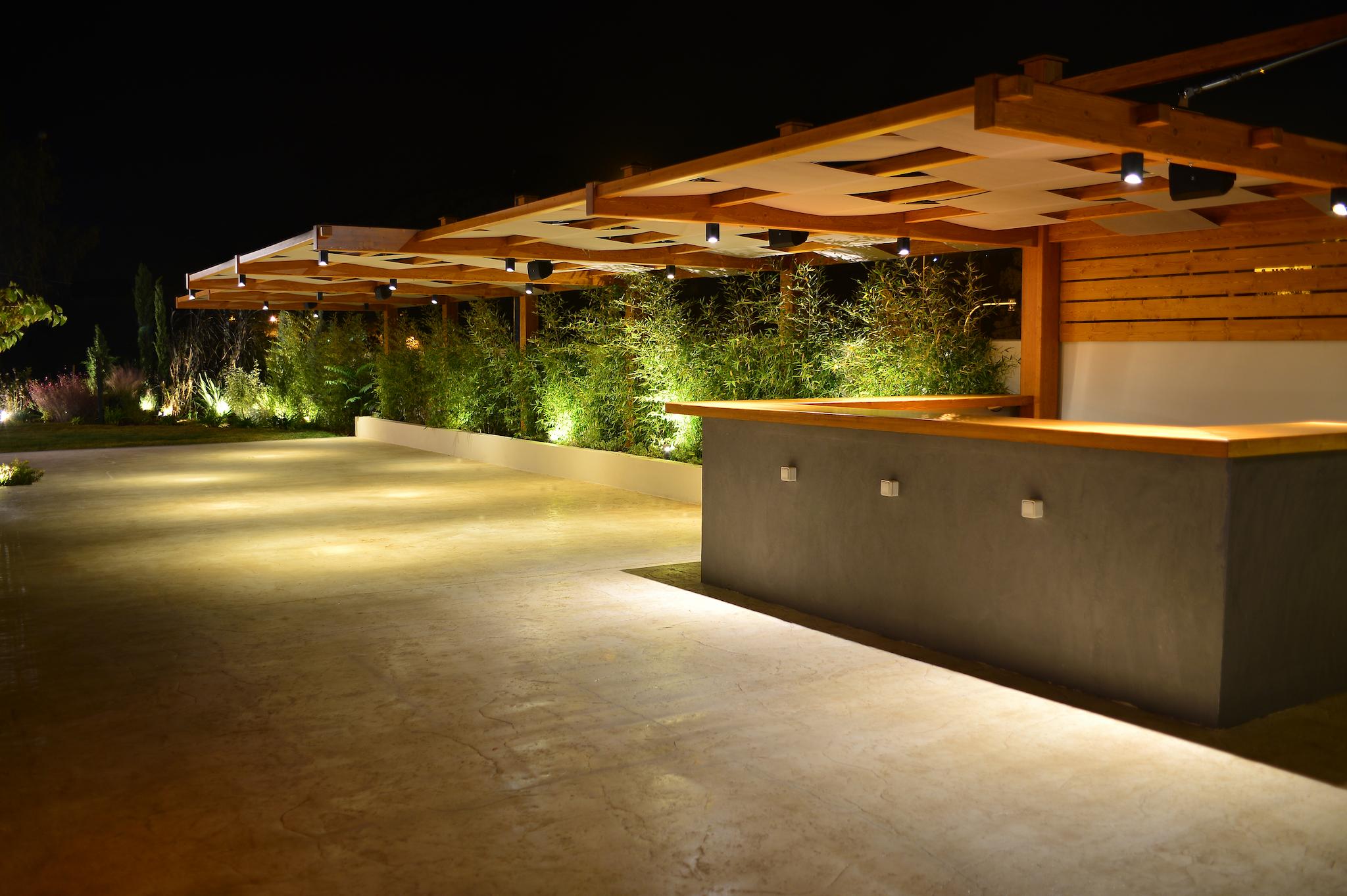 Ξύλινης κρεμαστή πέργκολα στο κτήμα με φόντο φυτά μπαμπού από πίσω. Φωτογραφία βραδινή με ανοιχτά τα φώτα