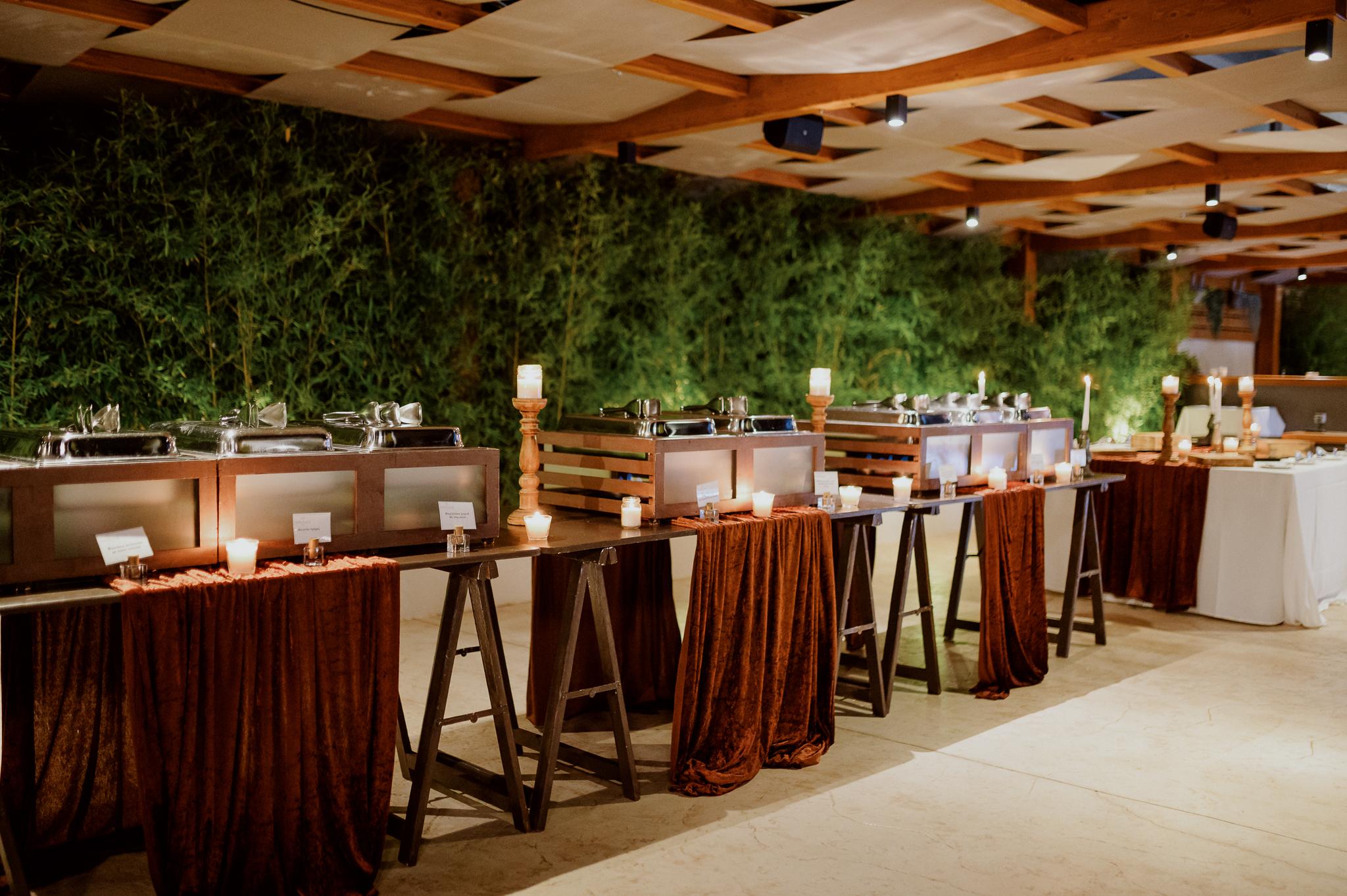 Πέργκολα ξύλινη που από κάτω έχει στρώση το catering τραπέζια με τα φαγητά επάνω.