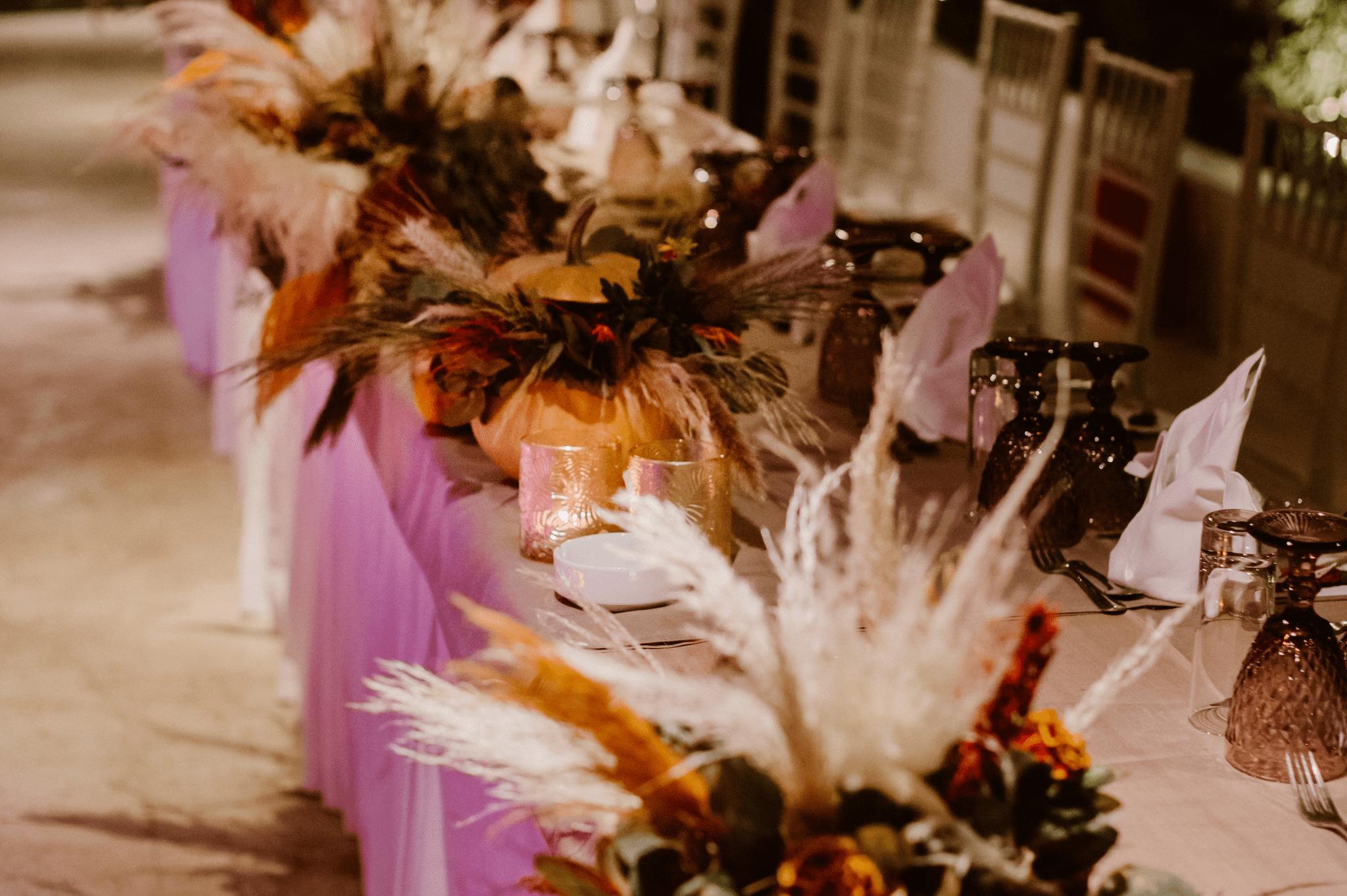 Κοντινή φωτογραφία από στολισμό νυφικού τραπεζιού . Ο στολισμός περιέχει pampas φυτά σε μπεζ και πορτοκαλί χρώμα με πράσινες λεπτομέρειες