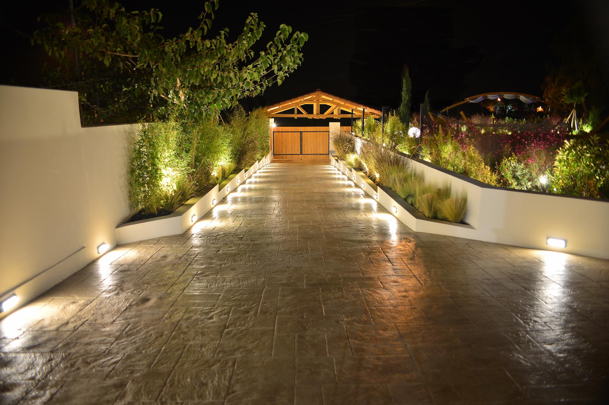 Είσοδος του κτήματος όπου φαίνεται ο διάδρομος και δεξιά και αριστερά φαίνονται τα πράσινα φυτά . Στο βάθος φαίνεται το στέγαστρο και η ξύλινη πόρτα.