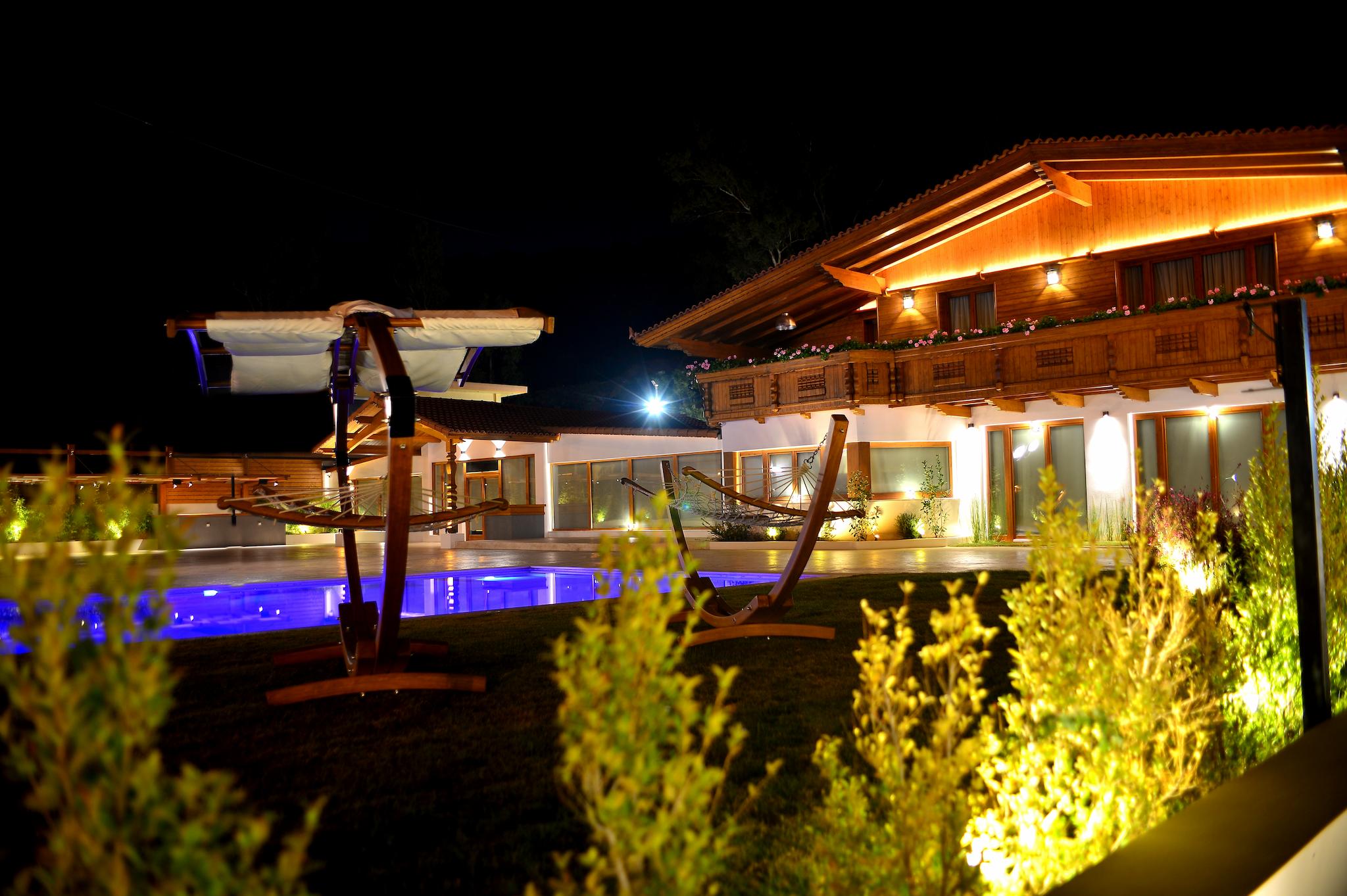 Φωτογραφία βραδινή η οποία φαίνεται το σπίτι το ελβετικό σαλέ φωτιζόμενο . Μπροστά από το οίκημα φαίνεται ο κήπος και τα φυτά του κτήματος