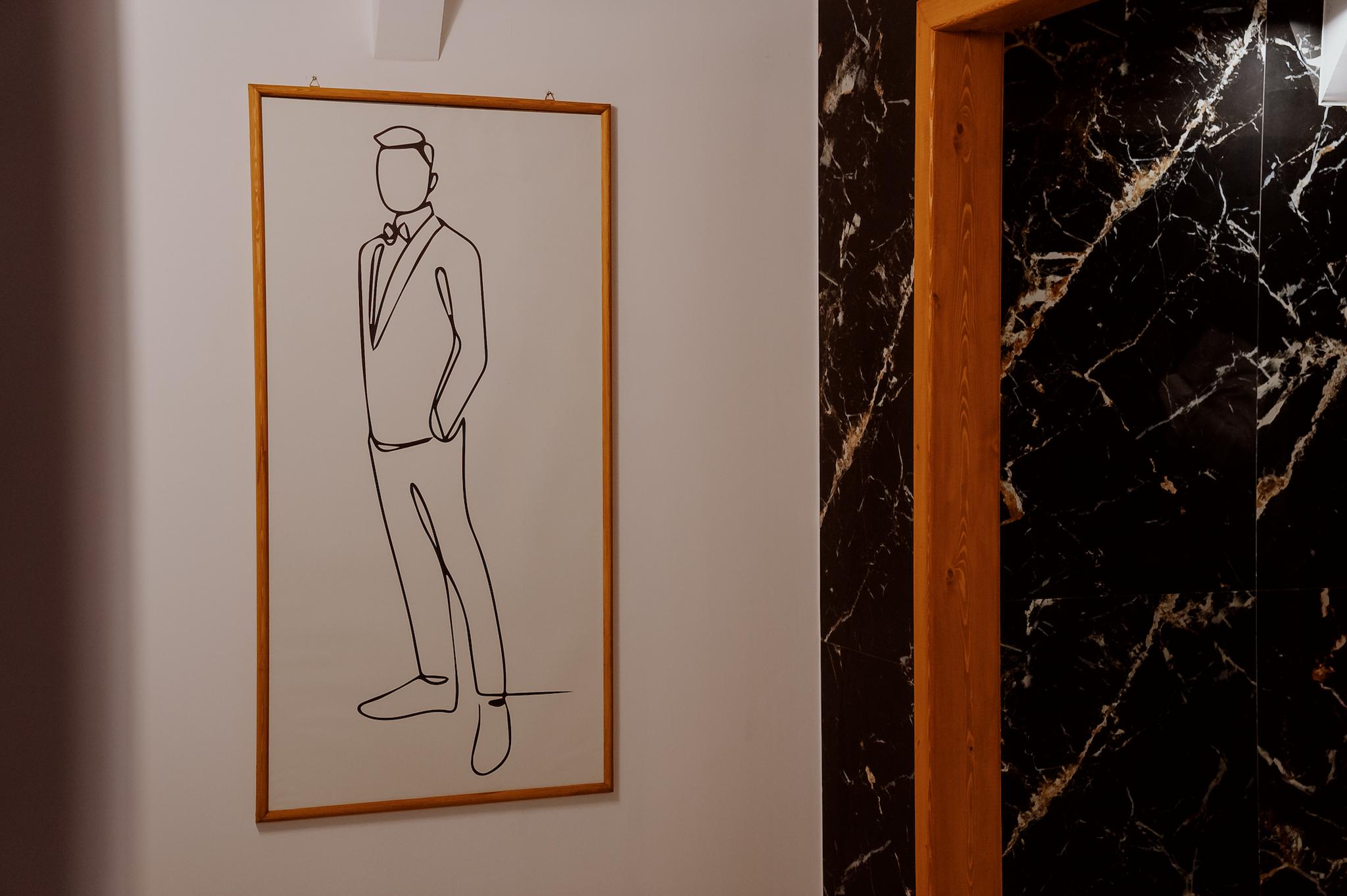 κοντινή λεπτομέρεια σε ένα κάδρο το οποίο απεικονίζει έναν άντρα με σκίτσο για την είσοδο στην τουαλέτα