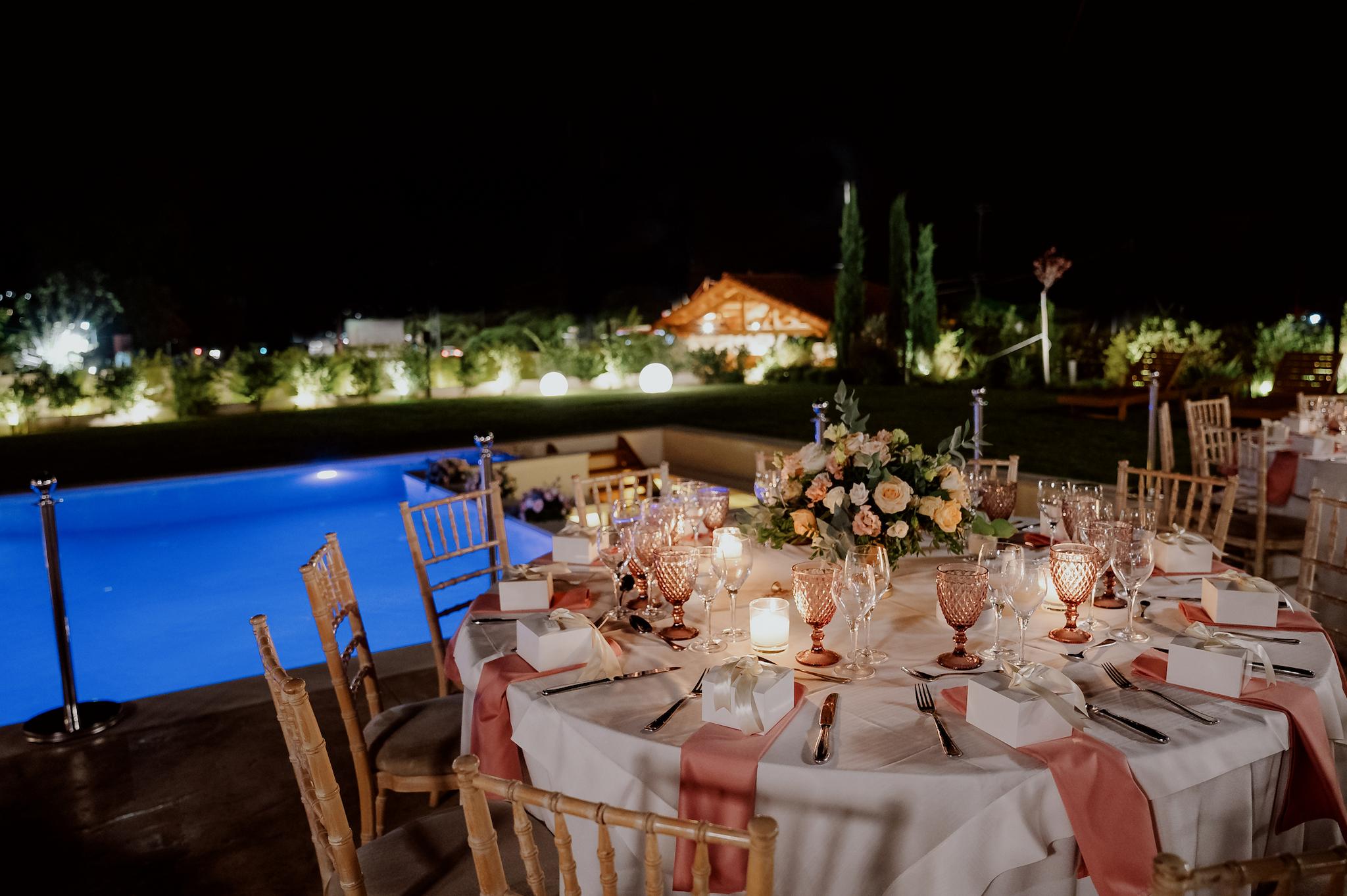 Στολισμός στα τραπέζια με τριαντάφυλλα σάπιο μήλο και λευκά με πολύχρωμα ποτήρια σε ροζ αποχρώσεις και καρέκλες tiffany στο βάθος φαίνεται το πολύχρωμα τοπίο από πράσινο και τα φυτά