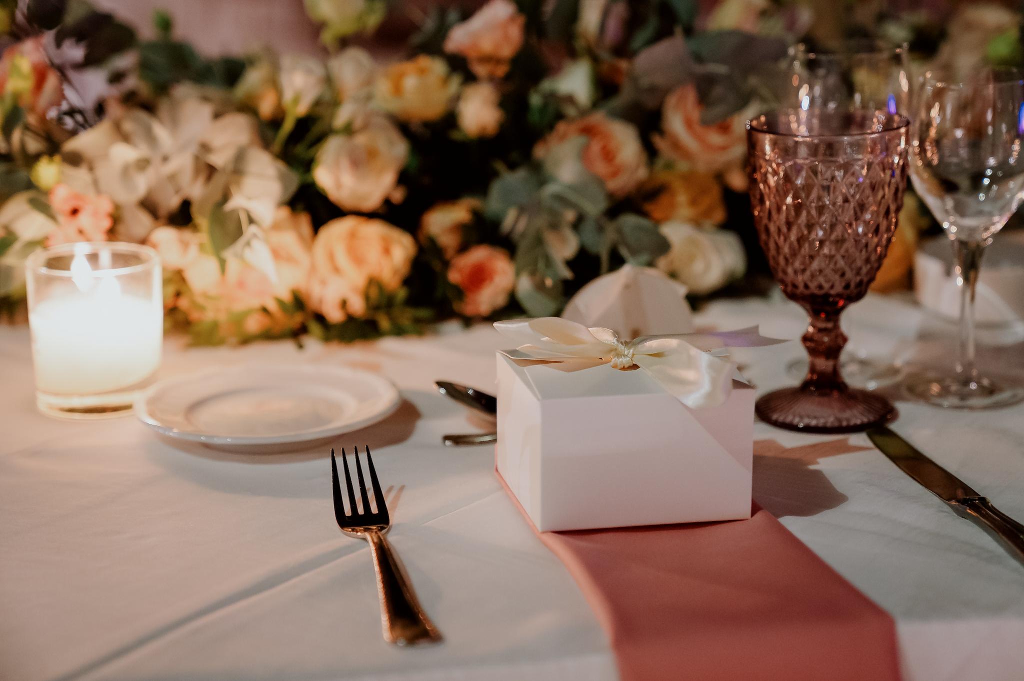 Κοντινή λήψη φωτογραφίας που απεικονίζει μπομπονιέρες επάνω στο τραπέζι στο κάθε άτομο ποτήρια από το catering μαχαιροπίρουνα στρωμένα τραπεζομάντηλα σε σομόν χρώμα