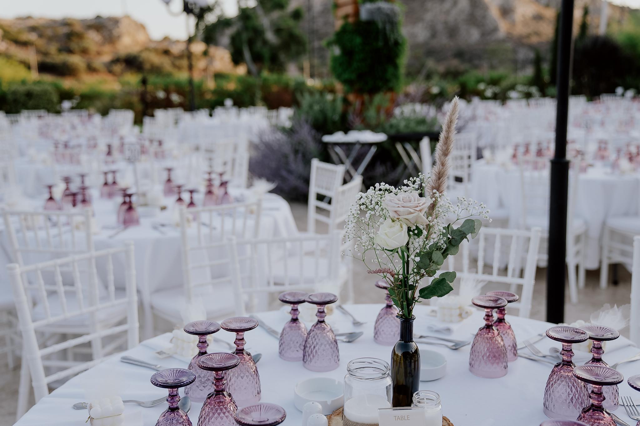 Κοντινό πλάνο με φόντο το πράσινο γκαζόν με φόντο τα φυτά. Οι ροτόντα είναι μισή και έχει tiffany καρέκλες και επάνω τα τραπέζια είναι στρωμένα