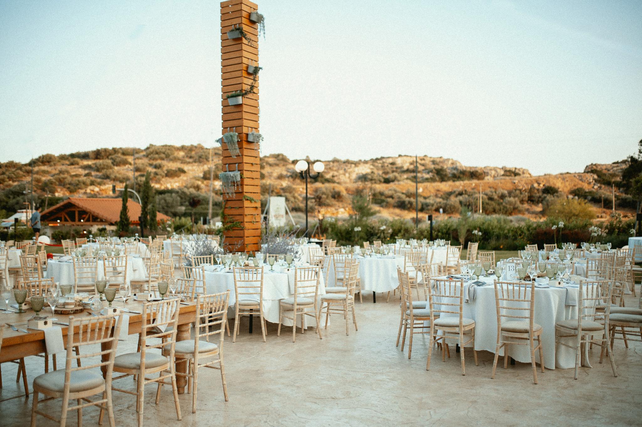 Εξωτερική φωτογραφία που φαίνονται τα τραπέζια και οι καρέκλες οι οποίες είναι tiffany ξύλινες .Φαίνονται τα μοναστηριακά τραπέζια και είναι στρωμένα με σερβίτσια στο βάθος φαίνεται το βουνό και ο πράσινος κήπος του κτήματος