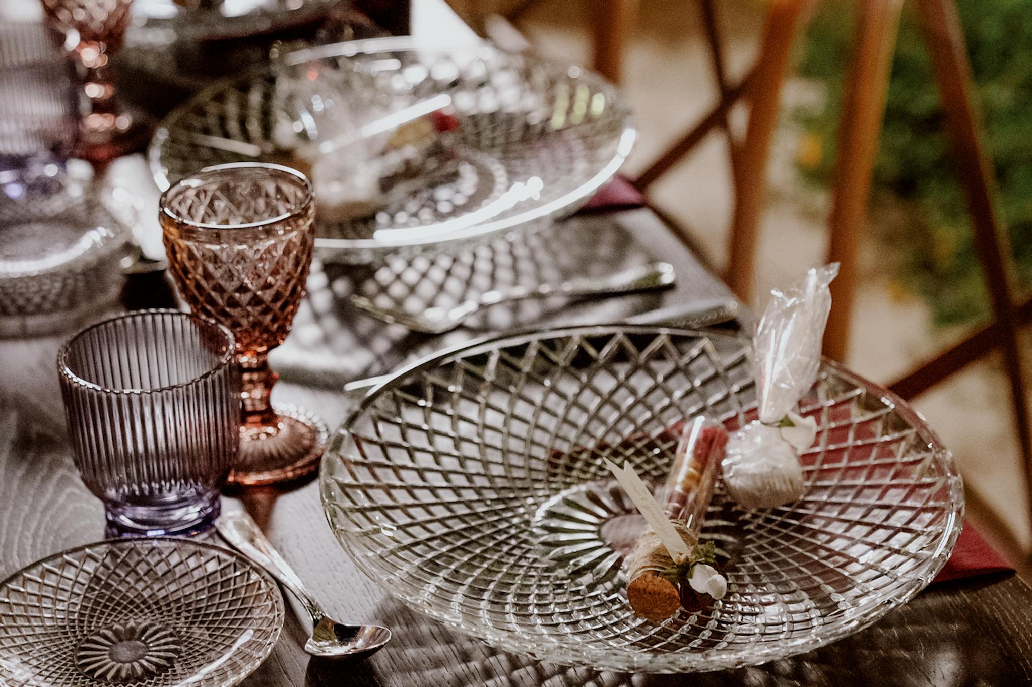 Κοντινή φωτογραφία με το μοναστηριακό τραπέζι το οποίο επάνω έχει στρώσει το catering σουπλα και από κάτω υπάρχει ατομική μπορντό πετσέτα και επάνω στο σουπλα υπάρχουν οι μπομπονιέρες και ένα γλυκο