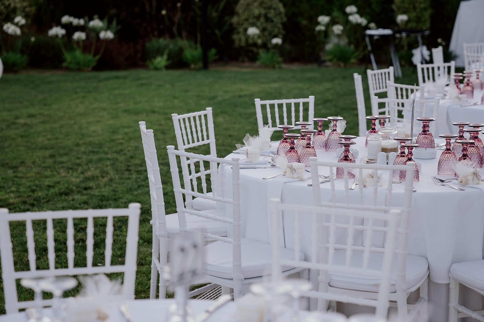 Κοντινό πλάνο με φόντο το πράσινο γκαζόν με φόντο τα φυτά. Οι ροτόντα είναι μισή και έχει tiffany καρέκλες και επάνω τα τραπέζια είναι στρωμένα