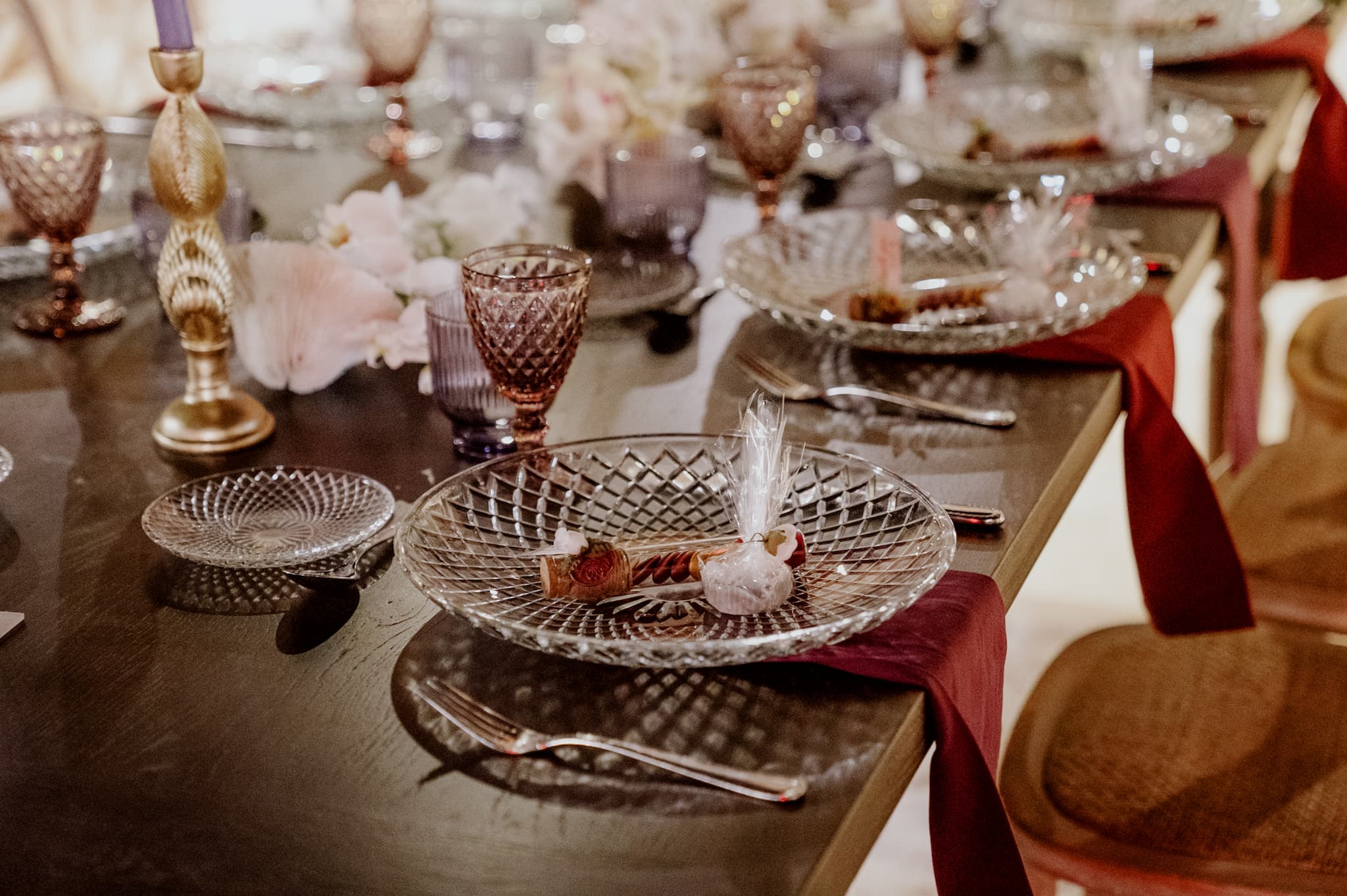 Κοντινή φωτογραφία με το μοναστηριακό τραπέζι το οποίο επάνω έχει στρώσει το catering σουπλα και από κάτω υπάρχει ατομική μπορντό πετσέτα και επάνω στο σουπλα υπάρχουν οι μπομπονιέρες και ένα γλυκο