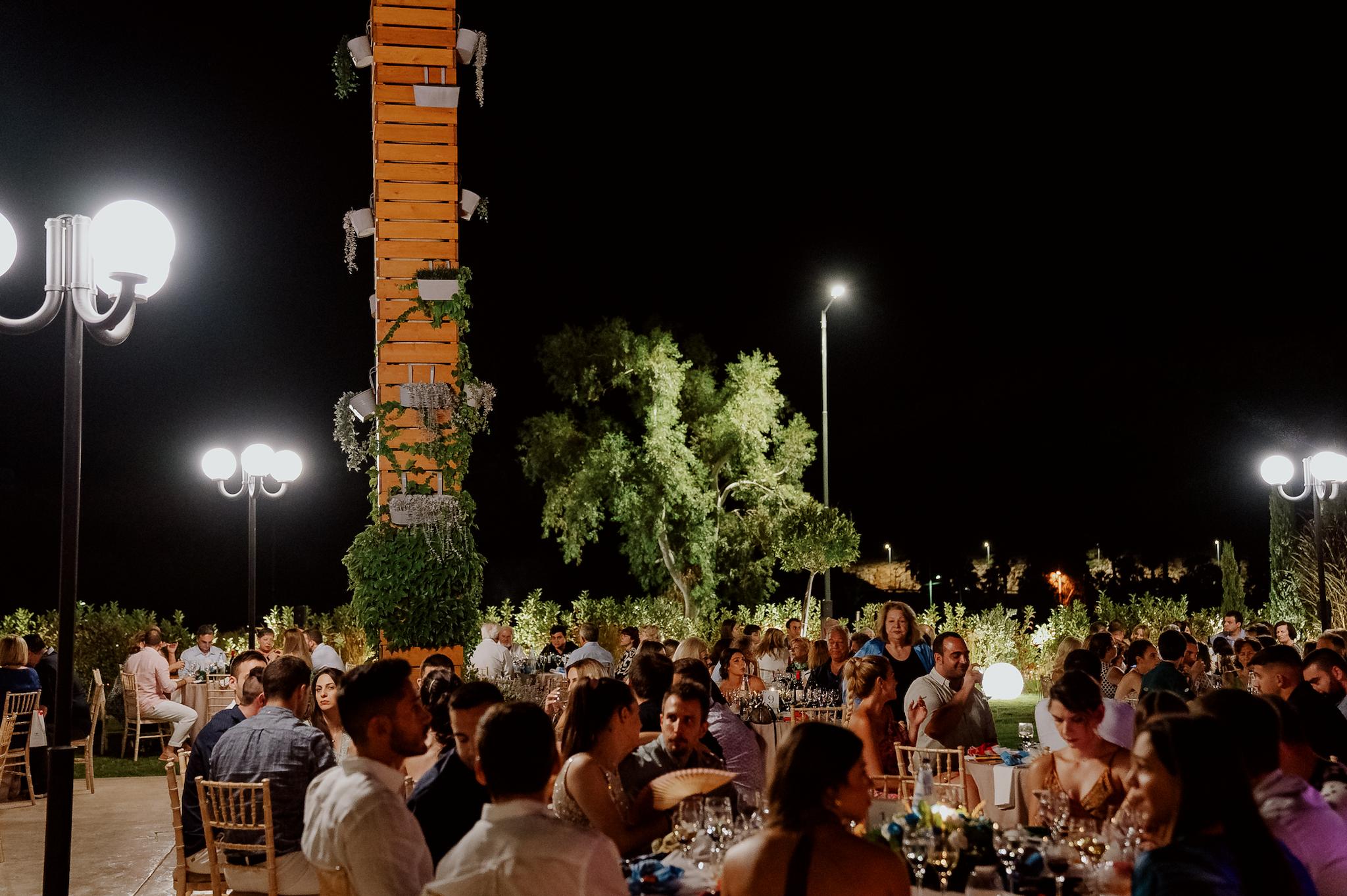 Βραδινή λήψη με ανθρώπους στο φόντο να κάθονται στα τραπέζια. Στο βάθος φαίνεται ο κήπος του κτήματος και το πράσινο.