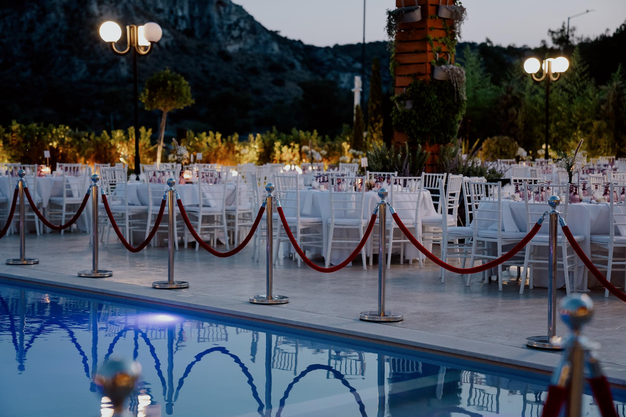 Η πισίνα του κτήματος με φόντο τις ροτόντες που είναι στρωμένες με τις καρέκλες περιμετρικά. Στο φόντο στο βάθος φαίνονται τα φυτά και ο κήπος